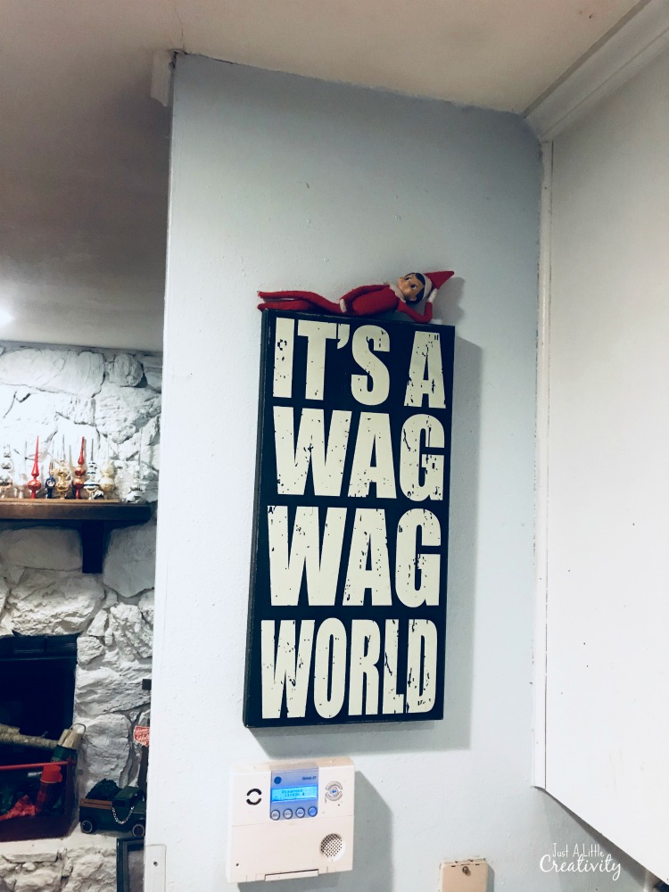 Elf on the shelf hiding on top of artwork